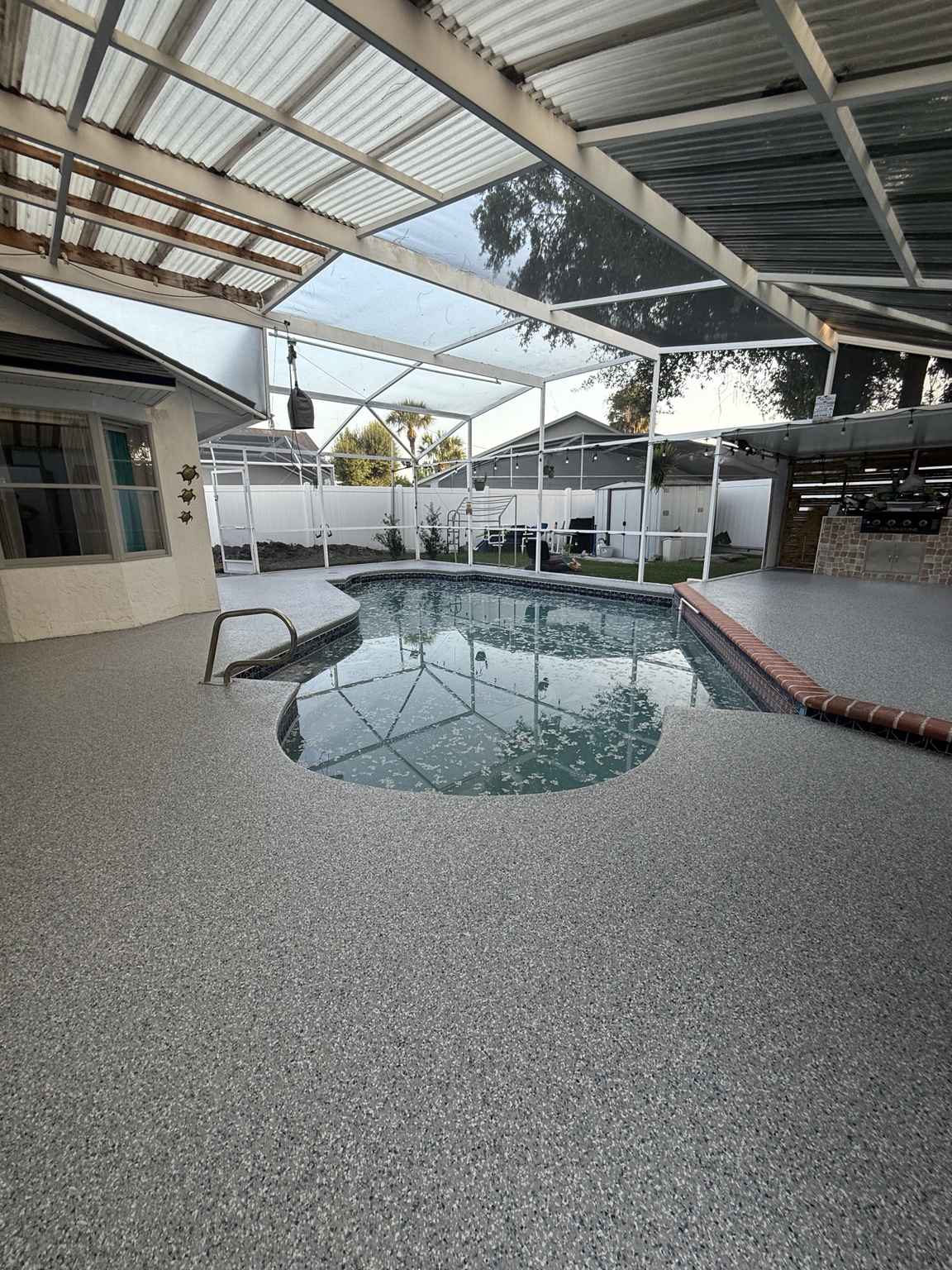 Gray full-flake concrete coating around a swimming pool inside a screened enclosure
