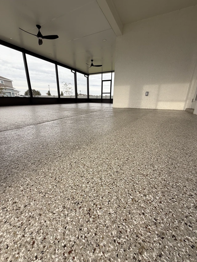Spacious screened lanai with two black ceiling fans and a decorative flake floor by EpoX Floor Coatings